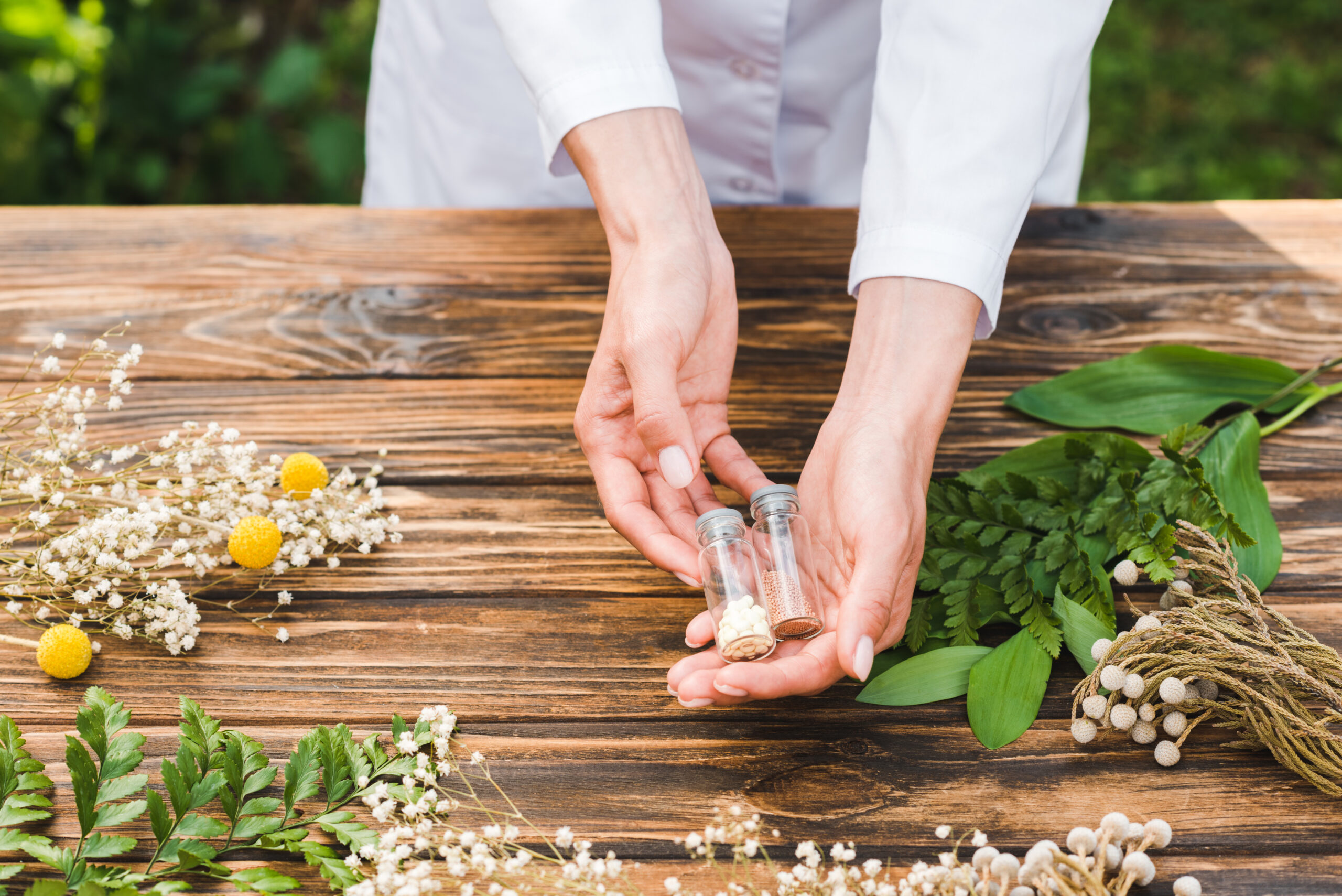 cropped view of woman holding glass bottles with pills near plants